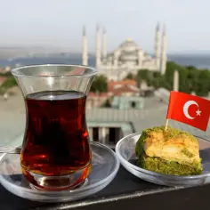 Szklanka tureckiej herbaty i baklava z turecką flagą na tle meczetu.
