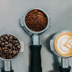 Trzy portafiltry: z ziarnami kawy, zmieloną kawą i latte art.
